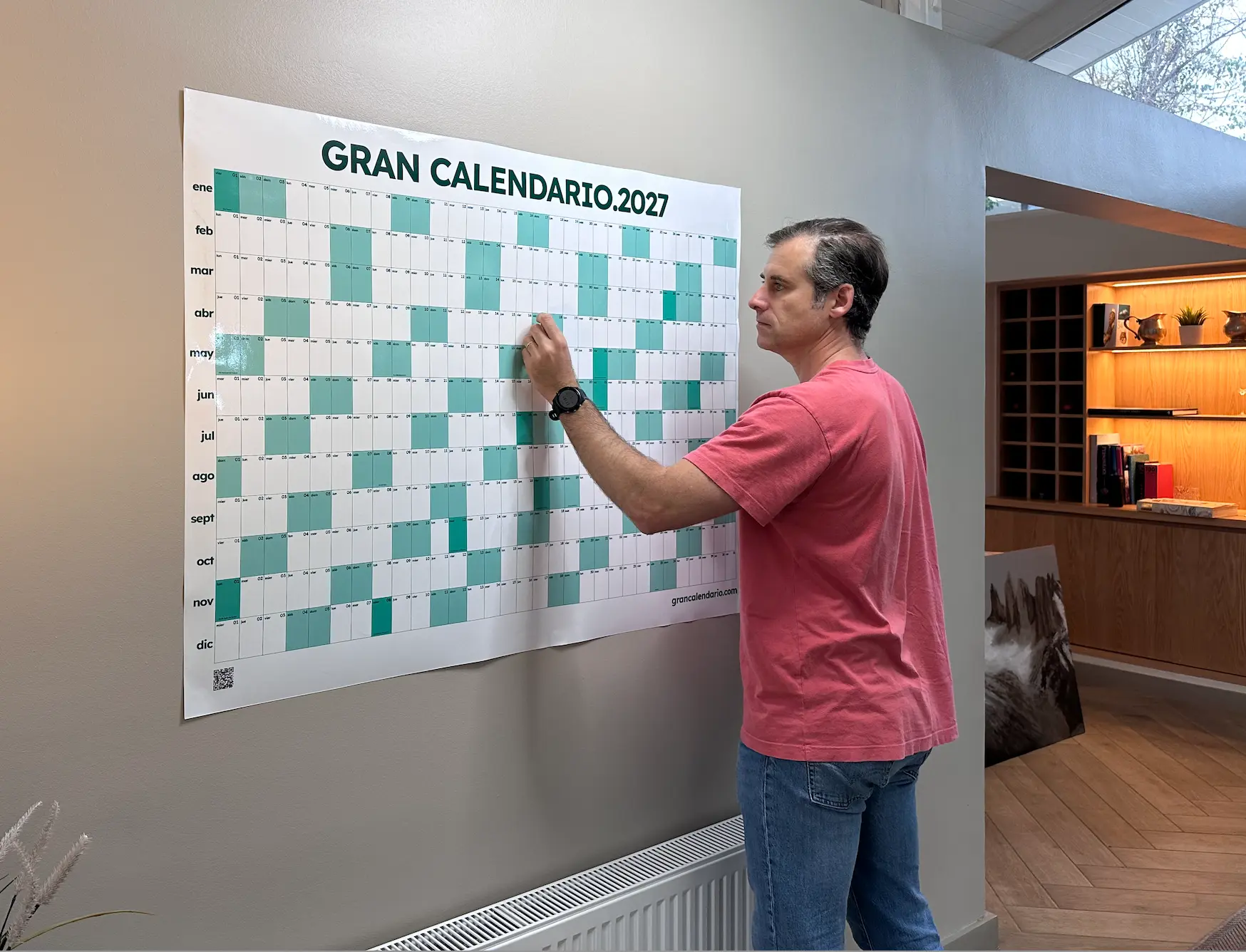 Hombre marcando fechas en el Gran Calendario 2027 colgado en la pared de su living